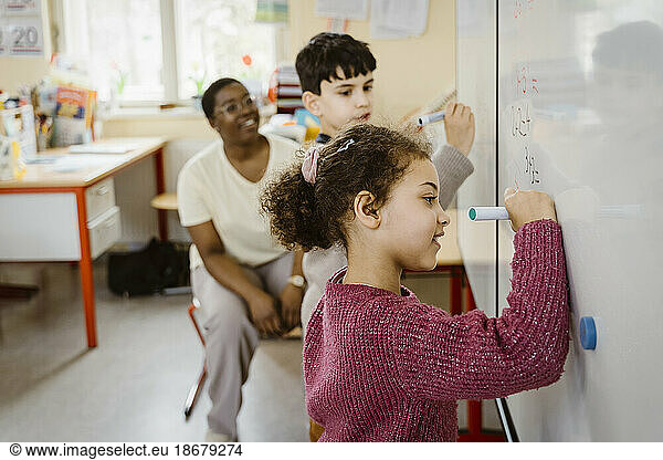 Mädchen und Junge schreiben auf der Tafel  während sie im Klassenzimmer mathematische Aufgaben lösen