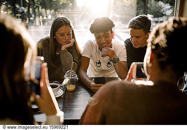 Mädchen und Jungen im Teenageralter nutzen soziale Medien auf Smartphones  während sie im Café sitzen