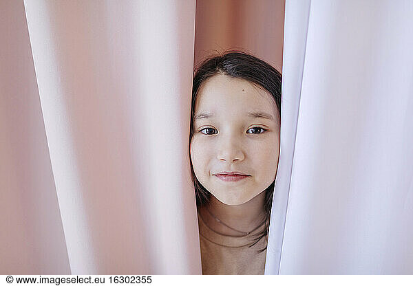Mädchen versteckt sich zu Hause hinter einem Vorhang