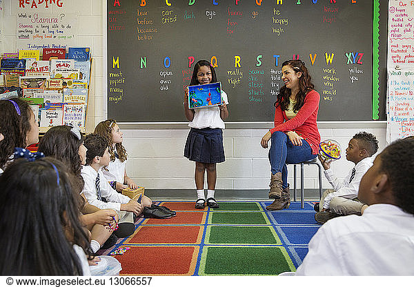 Mädchen zeigt Kunstwerke  während sie im Klassenzimmer steht