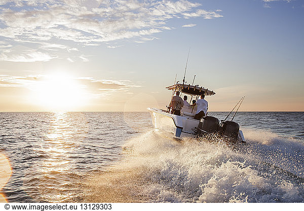 Männer genießen im Schnellboot auf See gegen den Himmel bei Sonnenuntergang