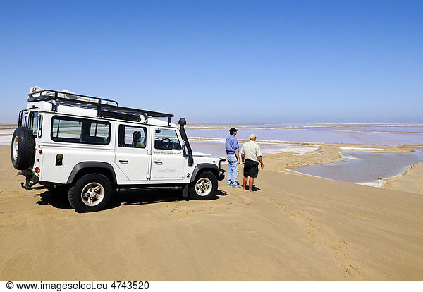 Männer mit Geländewagen Landrover Defender vor Wasserbecken zur Herstellung von Salz  Namib Naukluft Nationalpark  Teil des Namib-Skelettküste Nationalparks  Skeleton Coast  Wüste Namib  Namibia  Afrika