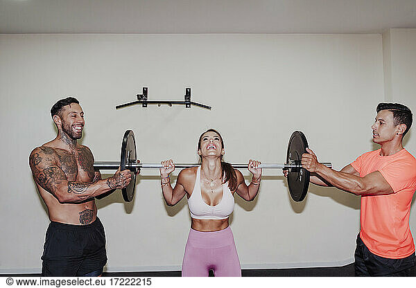 Männliche Athleten helfen einer Freundin beim Training mit der Langhantel im Fitnessstudio