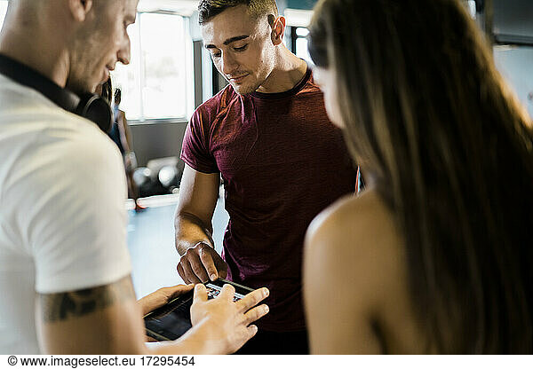 Männliche Athleten teilen sich ein digitales Tablet mit einer Freundin im Fitnessstudio
