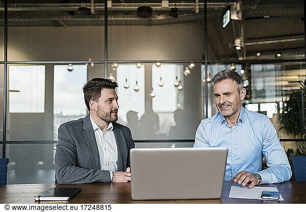 Männliche Fachleute arbeiten an einem Laptop  während sie im Sitzungssaal diskutieren