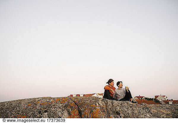 Männliche Freunde sitzen auf einem Felsen gegen den klaren Himmel