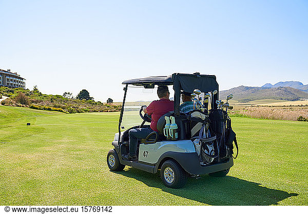 Männliche Golfer fahren Golfwagen auf sonnigen Golfplatzgrüns