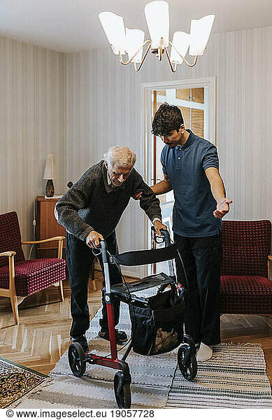Männliche Pflegekraft  die einen älteren Mann bei der Benutzung einer Gehhilfe zu Hause unterstützt
