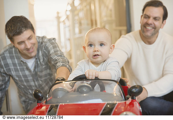 Männliche schwule Eltern schieben Baby Sohn in Spielzeugauto