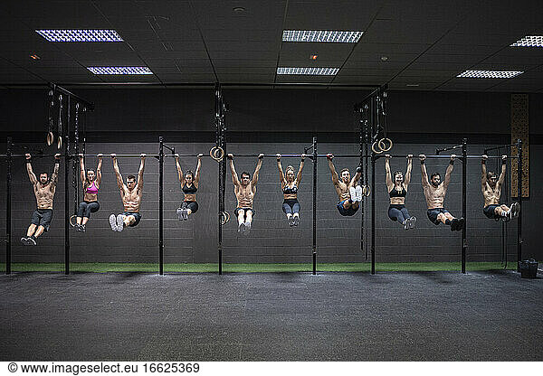 Männliche und weibliche Athleten hängen an einer Stange im Fitnessstudio