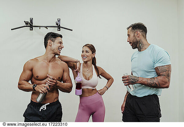 Männliche und weibliche Athleten im Gespräch vor einer weißen Wand im Fitnessstudio