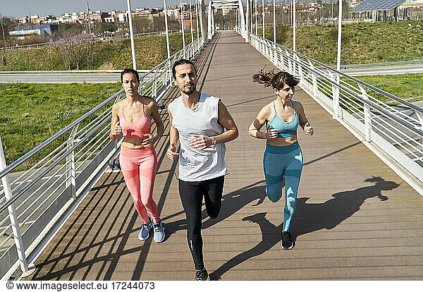 Männliche und weibliche Athleten schauen beim Laufen auf einer Brücke an einem sonnigen Tag weg