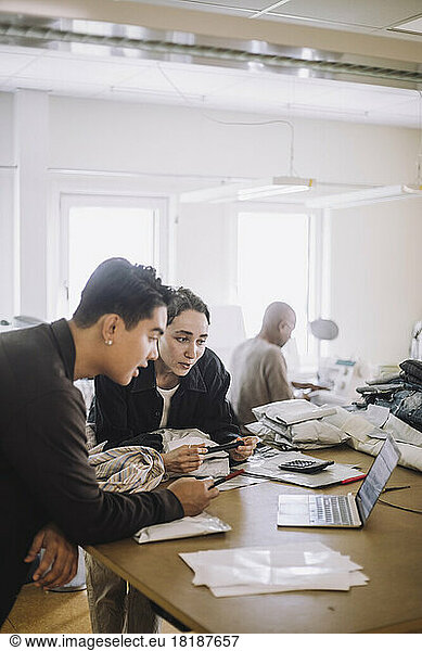 Männliche und weibliche Design-Profis schauen auf einen Laptop  während sie sich auf einer Werkbank in einer Werkstatt abstützen