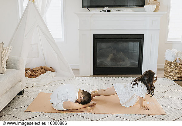 Männliche und weibliche Geschwister trainieren auf einer Matte im Wohnzimmer