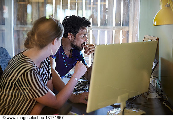 Männliche und weibliche Kollegen diskutieren am Computertisch im Kreativbüro