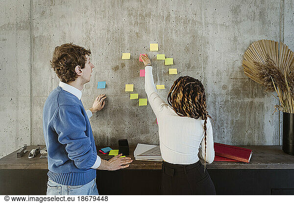 Männliche und weibliche Kollegen diskutieren über Haftnotizen an der Wand im Kreativbüro