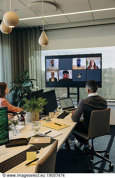 Männliche und weibliche Kollegen schauen während einer Videokonferenz in einem Coworking-Büro auf den Fernsehbildschirm