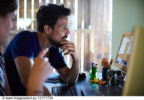 Männliche und weibliche Mitarbeiter diskutieren am Computerschreibtisch im Kreativbüro