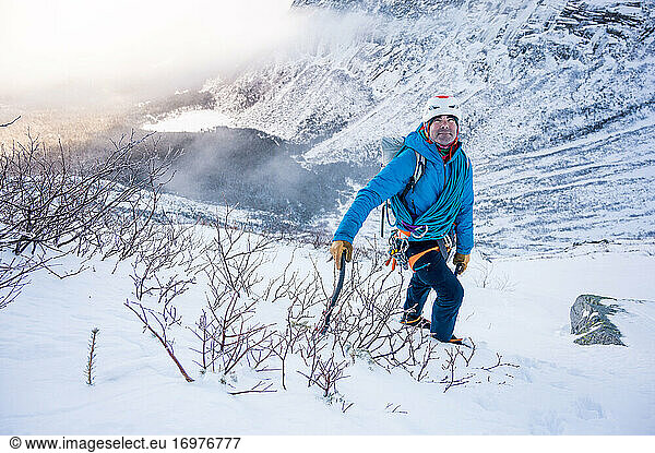 männlicher Alpinist steigt steiles Stück Schnee mit Bergen hinauf