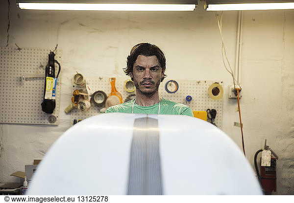 Männlicher Arbeiter betrachtet Surfbrett in Werkstatt