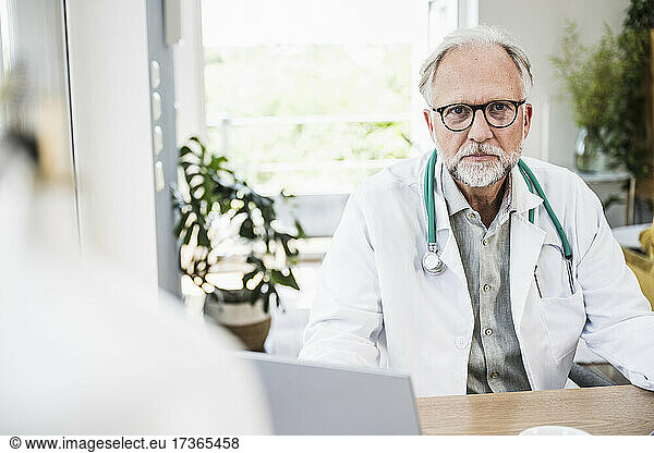 Männlicher Arzt mit Brille am Schreibtisch