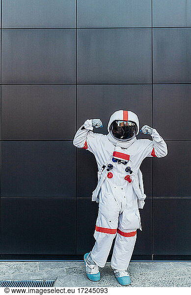 Männlicher Astronaut  der seinen Bizeps vor einer schwarzen Wand beugt