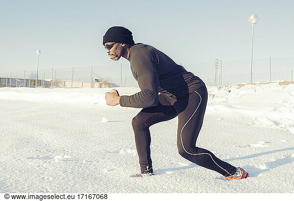 Männlicher Athlet  der an einem sonnigen Tag im Schnee läuft