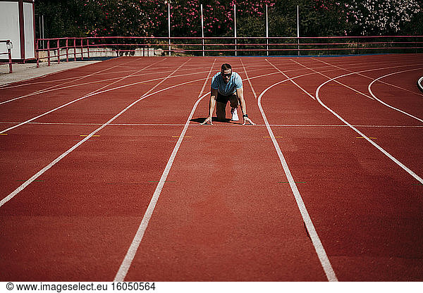 Männlicher Athlet in Startposition auf der Tartanbahn
