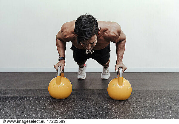 Männlicher Athlet macht Liegestütze auf einer gelben Kettlebell im Fitnessstudio