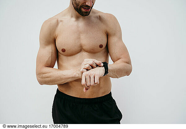 Männlicher Athlet mit nacktem Oberkörper überprüft seine Smartwatch