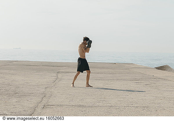 Männlicher Athlet ohne Hemd  der am Hafen stehend an einem sonnigen Tag Boxen übt