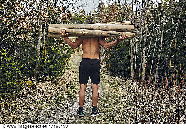 Männlicher Athlet ohne Hemd trägt Baumstämme im Wald