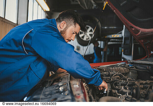 Männlicher Automechaniker in blauer Uniform repariert ein Auto