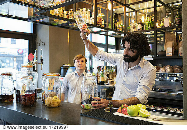 Männlicher Barkeeper gießt Alkohol in ein Fruchtglas am Bartresen