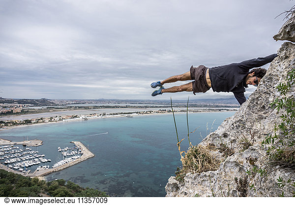 Männlicher Bergsteiger balanciert horizontal mitten in der Luft auf einem Küstenfelsen  Cagliari  Italien