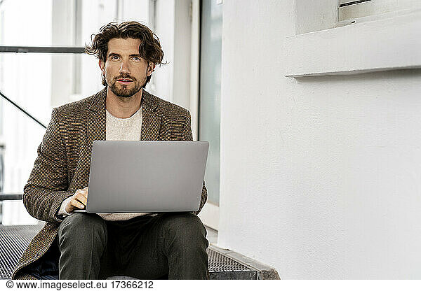 Männlicher Berufstätiger mit Laptop auf Stufen sitzend