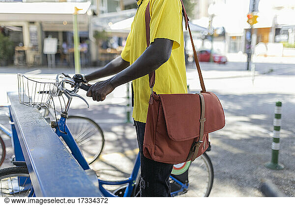 Männlicher Berufstätiger mit Umhängetasche parkt Fahrrad am Ständer