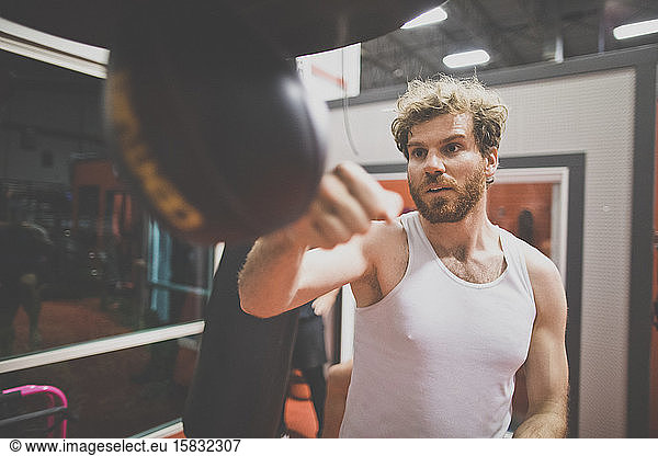Männlicher Boxer benutzt Boxsack in der Turnhalle