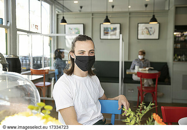 Männlicher Café-Besitzer mit Gesichtsschutzmaske  der wegschaut  während er während der Pandemie im Café sitzt