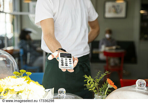 Männlicher Café-Besitzer zeigt Kreditkartenleser  während er im Café steht