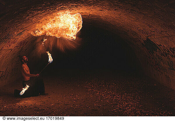 Männlicher Darsteller mit Feuerstab jonglierend im dunklen Tunnel