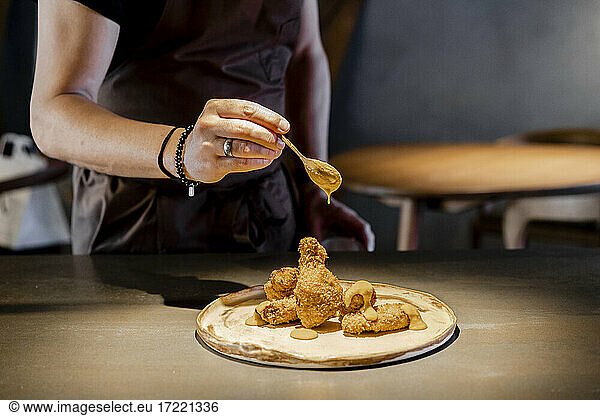 Männlicher Experte gießt Soße auf Chicken Nugget im Restaurant