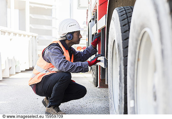 Männlicher Ingenieur mit Schutzhelm und Gehörschutz  der das Fahrgestell eines Lastwagens überprüft.