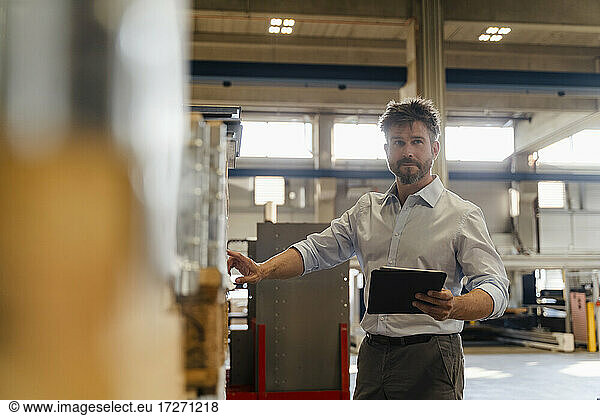 Männlicher Inspektor  der ein digitales Tablet benutzt  während er Material im Lager einer Fabrik überprüft