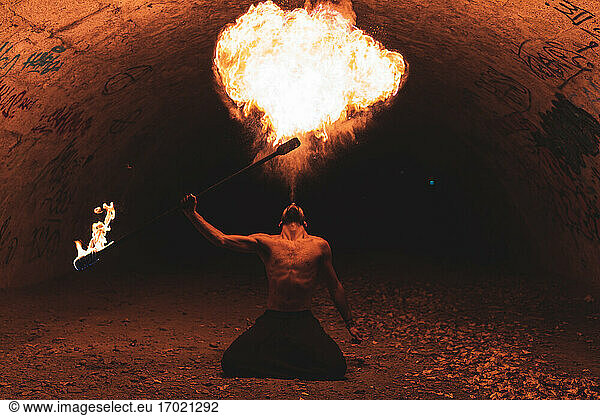 Männlicher Jongleur mit Feuerstab im dunklen Tunnel