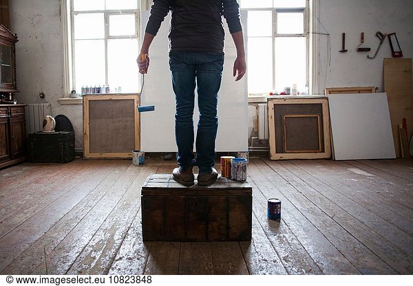 Männlicher Künstler auf Kiste sitzend  auf leere Leinwand schauend  niedriger Schnitt