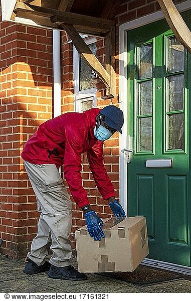 Männlicher Kurier  der während der Covid-19-Epidemie Pakete und Päckchen ausliefert und dabei Handschuhe und einen Mundschutz trägt  Hampshire  England  Vereinigtes Königreich.