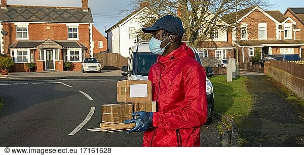 Männlicher Kurier  der während der Covid-19-Epidemie Pakete und Päckchen ausliefert und dabei Handschuhe und einen Mundschutz trägt  Hampshire  England  Vereinigtes Königreich.