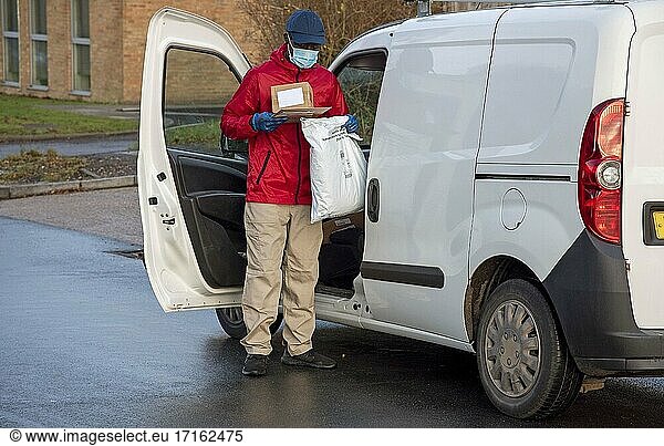 Männlicher Kurier  der während der Covid-19-Epidemie Pakete und Päckchen ausliefert und dabei Handschuhe und einen Mundschutz trägt  Hampshire  England  Vereinigtes Königreich.