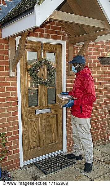 Männlicher Kurier  der während der Covid-19-Epidemie Pakete und Päckchen ausliefert und dabei Handschuhe und einen Mundschutz trägt  Hampshire  England  Vereinigtes Königreich.